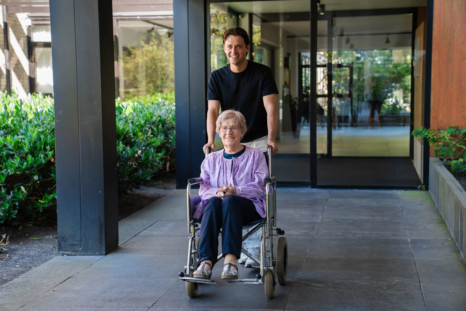 Een jonge gezelschap aanbieder maakt een wandeling met een senior vrouw in een rolstoel